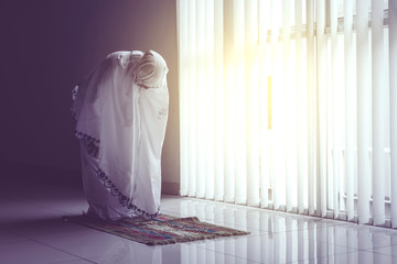 Woman doing salat at home with praying veil and mat