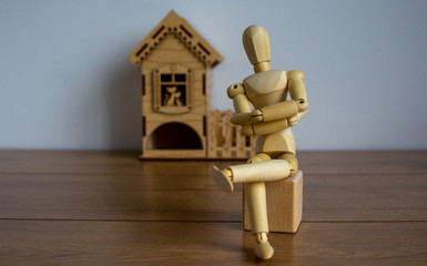 Wooden model of a sitting man in front of a miniature house.