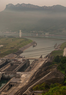 Three Gorges Dam, China - May 6, 2010: Yangtze River. Foggy smog morning,  Portrait of Xiling suspension bridge over river and canal coming from ship lift. Mountains and buildings on horizon.