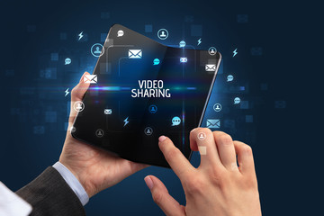 Businessman holding a foldable smartphone with VIDEO SHARING inscription, social networking concept