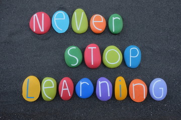 Never Stop  Learning, motivational slogan composed with multi colored stone letters over black volcanic sand