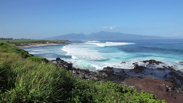 Ho'okipa State Park on Maui with large white waves rolling to shore with the West Maui Mountains and blue sky in the background on a sunny Hawaii day.