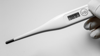 hands holding white digital thermometer on white background. Showed 38.9 c’. Fever and healthcare concept. Cover-19 test.  healthcare concept