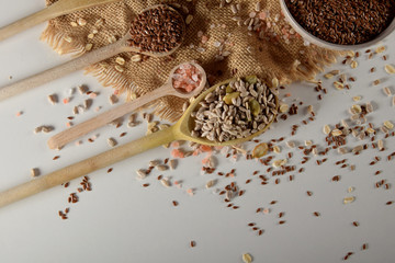 Obraz na płótnie Canvas wooden spoon full of sunflower seeds and pumpkin seeds next to wooden spoons with linseed and pink salt