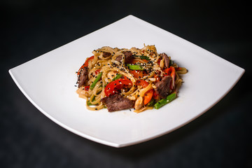 Pad Thai of vegetables and meat on a white plate on a black background