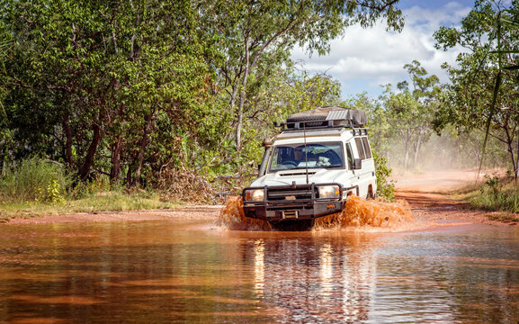 Western Australia – Flooded Outback gravel road with 4WD car crossing the waterhole with splashing muddy water at the savanna