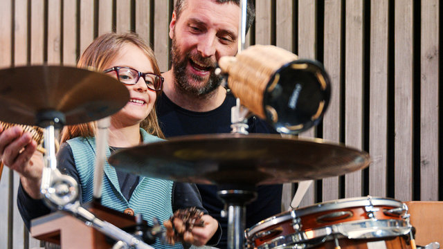 Father And Daughter Enjoy Play Music Together.Little Girl Smiling Learning Drums With Her Dad At Home.Front View.Percussion Class At Home