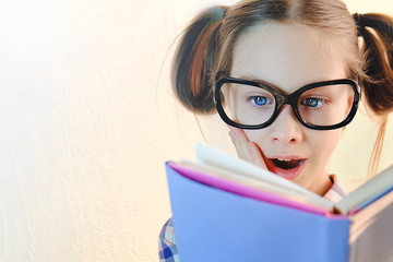 Girl schoolgirl with glasses on her face with delight reads a book