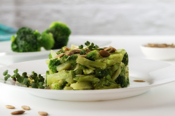 Boiled broccoli with pumpkin seeds on a white plate on the table