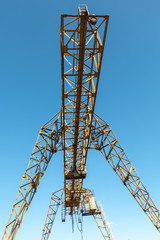 Vintage working gantry crane rusty yellow, bottom view, close-up against a blue spring sky