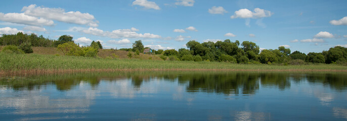 A small holiday house on the shore of a picturesque lake. Blue skies with white clouds.