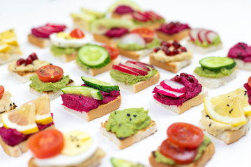 Fototapeta na wymiar set of different bruschetta sandwiches with beet hummus, guacamole, different vegetables. vegetarian helsifood concept. summer snack. food patern on white background