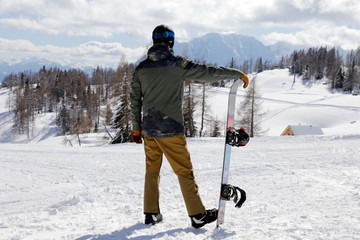 Young man standing and enjoying the view. Man standing with snowboard on winter holiday. Winter...