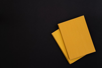 Two hardcover yellow books on a black background. Copy space. Dark mode style. Top view. Minimal concept