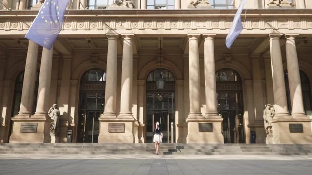 Frankfurt, Germany, April 8, 2020 Young women on phone waering protective face mask against corona virus covid-19 walking in front of the stock market exchange shot in 4k