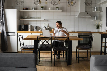 Young freelancer succeed with project working from home. Excited glad young freelancer triumphing...