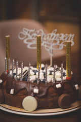 A close-up of chocolate birthday cake. Holiday treat. Healthy cake for a child, decorated with candles and fireworks with the word in Russian - Congratulations, in the background. Toning