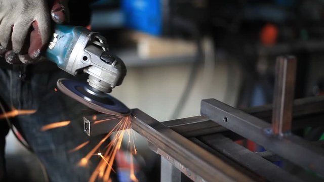 Grinding metal profile. Work as a grinder in a workshop. Sparks from steel processing. A rotating disc sharpens steel. An electric tool in the hands of a worker. Male labor. Creating a design.