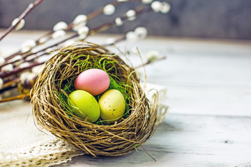 A nest of Easter eggs of different colors on a light wooden table surrounded by twigs of willow and quail eggs. Copy Space Greeting Card Easter Concept, Top view, flat lay