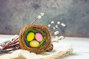 A nest of Easter eggs of different colors on a light wooden table surrounded by twigs of willow and quail eggs. Copy Space Greeting Card Easter Concept, Top view, flat lay