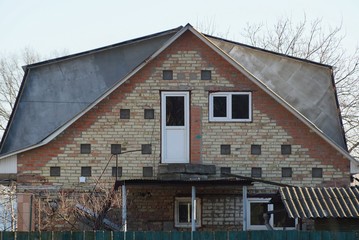 brown brick facade of a rural house with a white window and a door against the sky