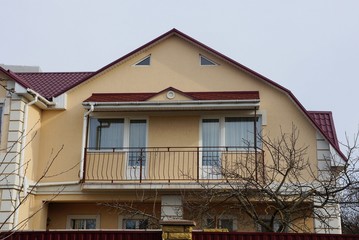 facade of a brown private house with an open black iron balcony against a gray sky