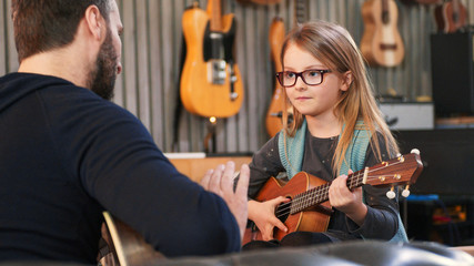 Fototapeta Dad teaching guitar and ukulele to his daughter.Little girl learning guitar at home.Close up.Ukulele class at home. Child learning guitar from her father obraz