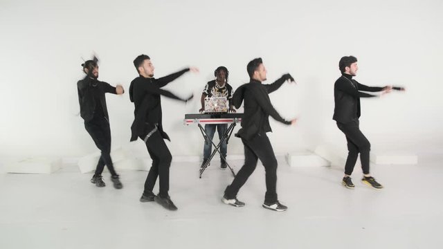 Group of young modern dancers dancing in the white studio. Sport, dancing and urban culture concept,behind them is a black DJ