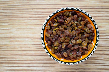 Top view raisins in a bowl on a wooden table.