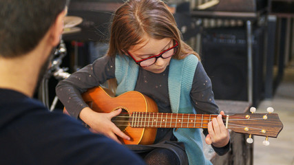 Dad teaching guitar and ukulele to his daughter.Little girl learning guitar at home.Close up.Ukulele class at home. Child learning guitar from her father - obrazy, fototapety, plakaty
