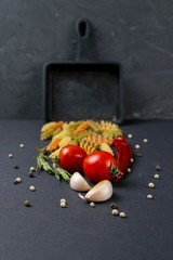 Italian food raw pasta fusilli with tomatoes, rosemary, hot pepper and garlic in a small frying pan