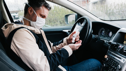 a man in a medical mask rubs his hands with a sanitizer in a car close view