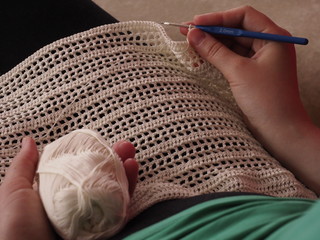 A girl crochets a dress made of thread. A woman works with delicate lace