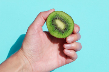 Imagen de una mano con un medio kiwi verde con fondo azul brillante