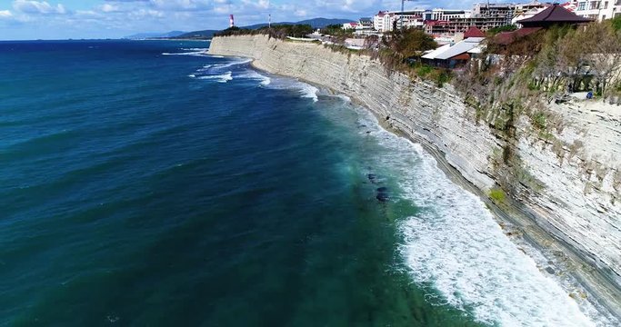 Drone flight along The black sea coastline. High rocky cliff. A strip of shingle beach below. In the distance, the lighthouse of Gelendzhik. 