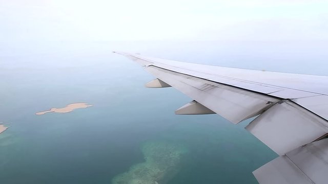 airplane wing on window view during taking off from Hamad International Airport runway, Aerial shot at a low height of artificial islands on the sea.