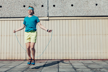 Young teenager boy jumping by the skipping rope on the house roof. Modern people fit challenges...