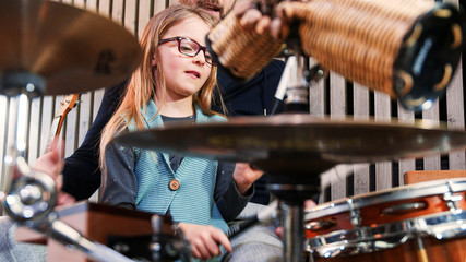 Father and daughter play percussion together.Little girl learning drums with her dad at home.Front view close up.Percussion class at home