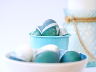 Blue, green, turquoise and white homemade easter eggs colored with a red cabbage natural colour on a white background with blank space decorated with spring flowers in a bowl closeup.