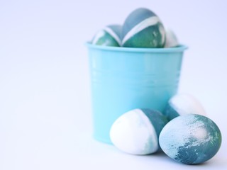 Blue, green, turquoise and white homemade easter eggs colored with a red cabbage natural colour on a white background with blank space decorated with spring flowers in a bowl closeup.