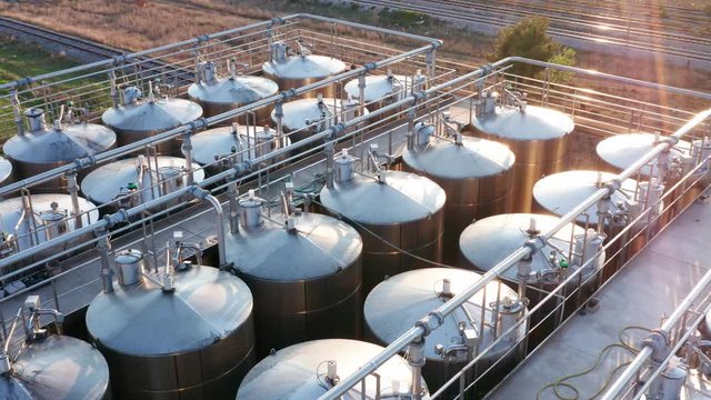 Industrial pipes in factory - stainless steel tanks. Shiny silos in a chemical industry plant. Metal containers with hazardous chemicals. Aerial footage.