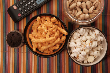 A bowl of popcorn chips, nut and TV remote,