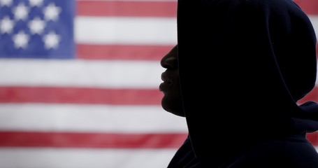 CU silhouetted African American man in a  hoodie, face in profile, with US flag in background