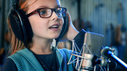 Kid singing in studio.Little girl singing a song.Front view close up. Kid wearing headphones...