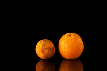 Two oranges in dark background with reflection. Fresh and spoiled. Concept- Freshness and withering, youth and old age. Beautiful and ugly fruits