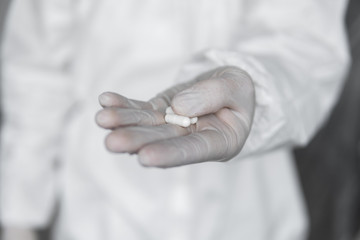 Doctor in white protective suit, medical mask and rubber gloves is holding a white pills as a medications from coronavirus pandemic threat. Epidemic, pandemic of coronavirus covid 19.