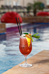 Refreshing cocktail with ice cubes perfect for outdoor event. Fancy beverage decoration with crafted leaf, lemon sliced and orange zest. Pool side area in hotel.