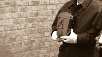 Funeral director or undertaker carrying a smooth metal urn in his hands, filled with ash towards...