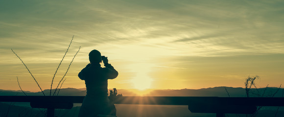 Female hiker on top of the hill taking a picture of a sun at a sunrise. Early trek to a summit and taking a photo. Concept of early and beautiful outdoors.