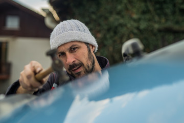 Auto repair worker straightening dents in metal car sheet or body using a hammer. Special body...